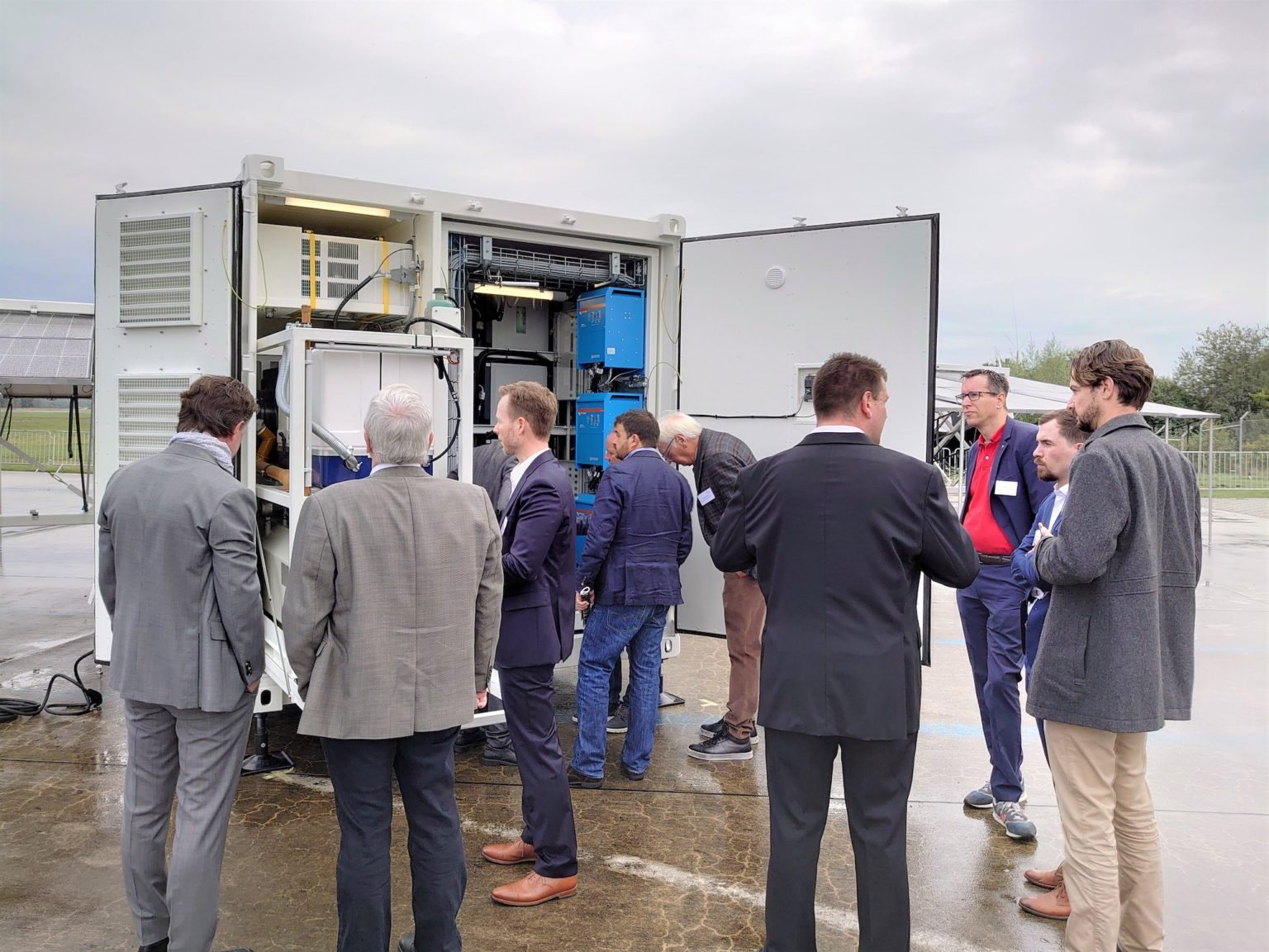 Opslagcontainer met open deuren, Victron-omvormers zichtbaar, ondernemers ervoor tijdens een presentatie